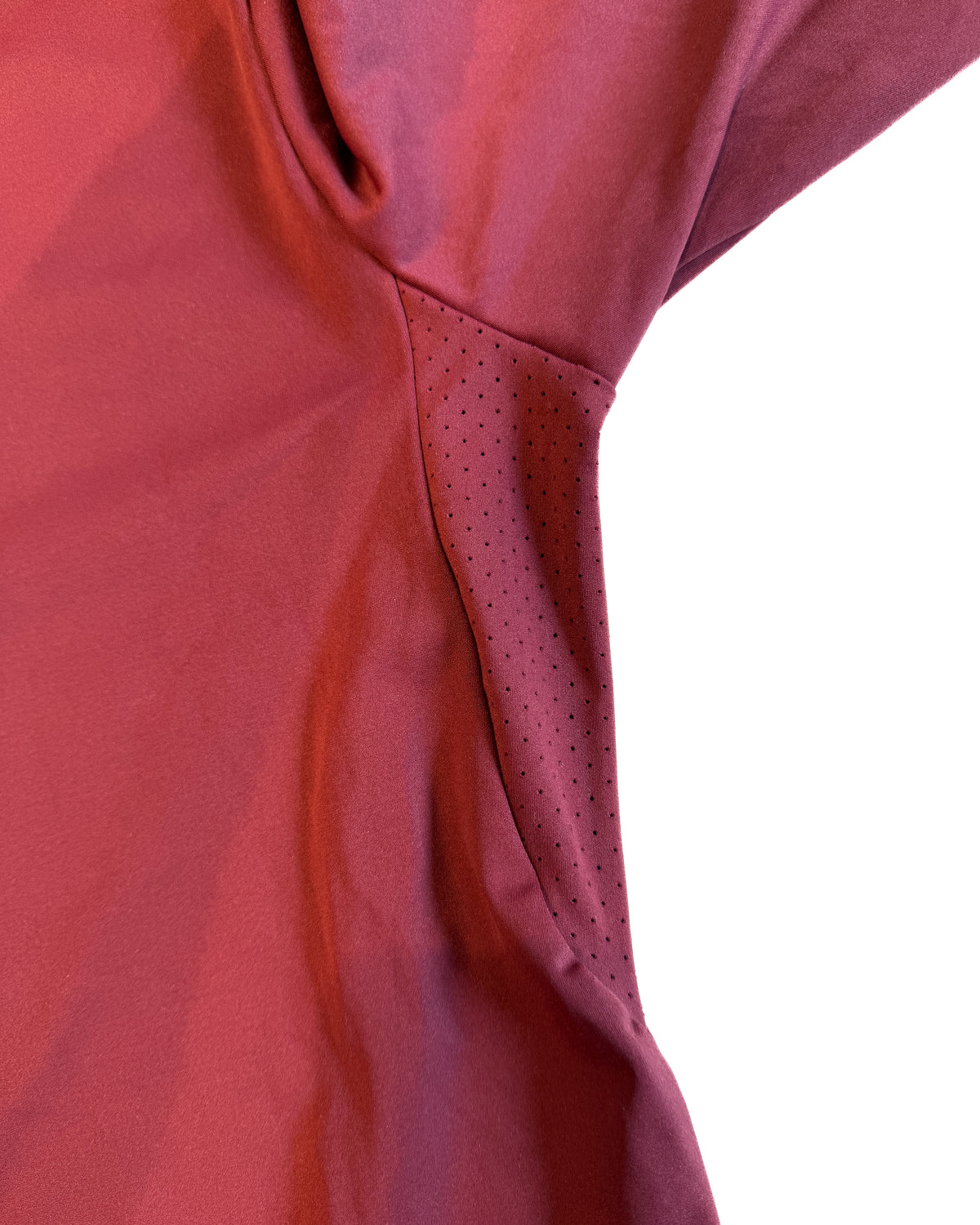 Close-up of a red athletic top showing the shoulder and side seam with a perforated mesh detail, set against a plain white background.